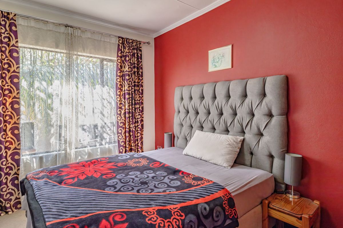 A bedroom featuring a bold red accent wall, large window with natural light, and classic coving detail.