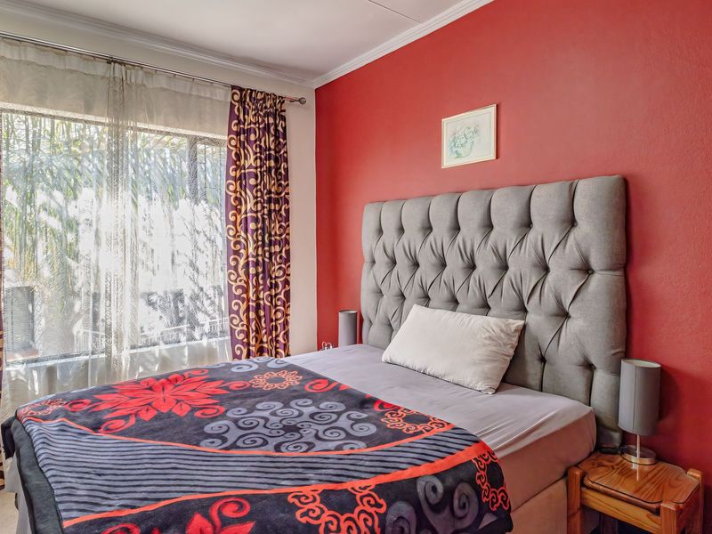 A bedroom featuring a bold red accent wall, large window with natural light, and classic coving detail.