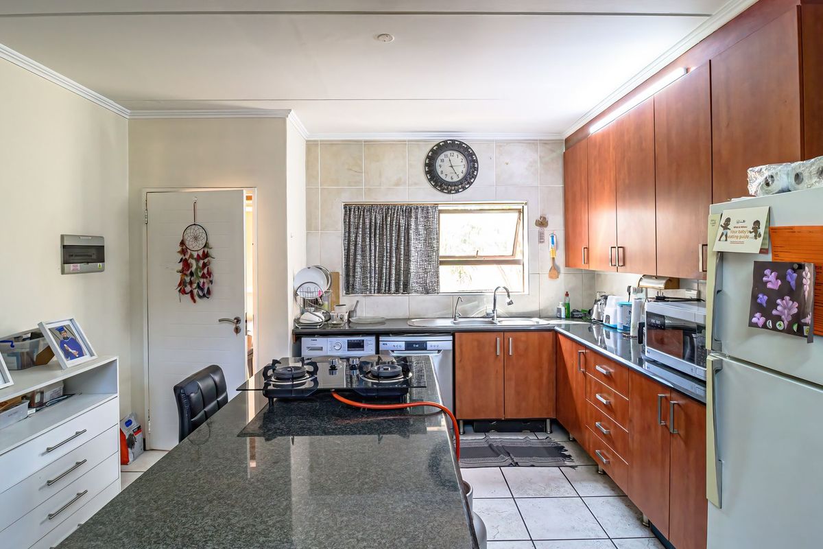 A functional kitchen featuring granite countertops, wooden cabinetry, a gas hob, and tiled flooring, offering a practical layout for daily cooking and preparation.