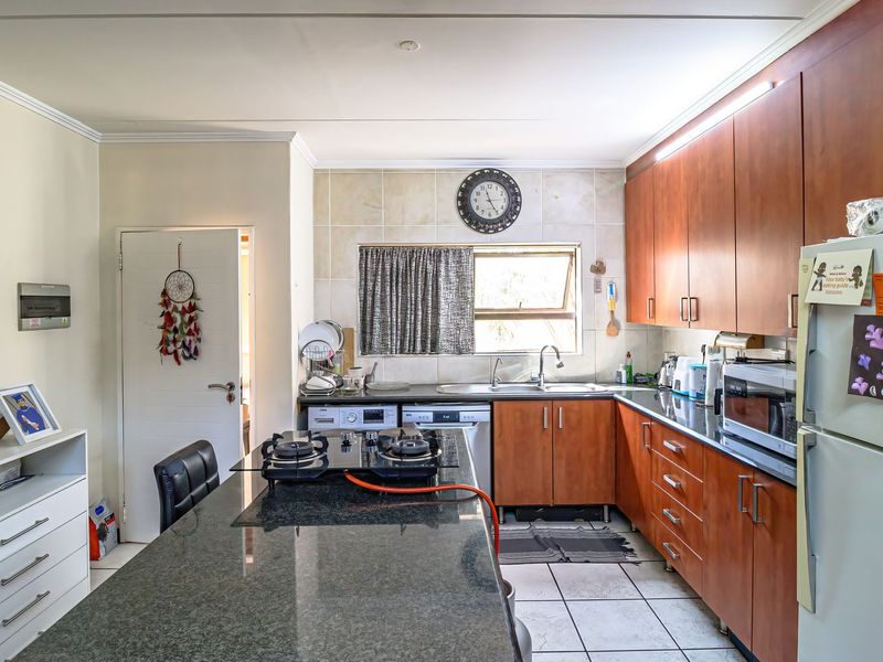 A functional kitchen featuring granite countertops, wooden cabinetry, a gas hob, and tiled flooring, offering a practical layout for daily cooking and preparation.