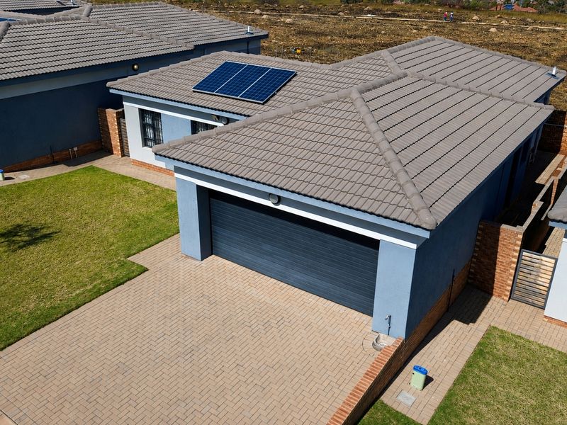 Aerial view of a modern residential property featuring a tiled roof with solar panels, a paved driveway, and a private garage.