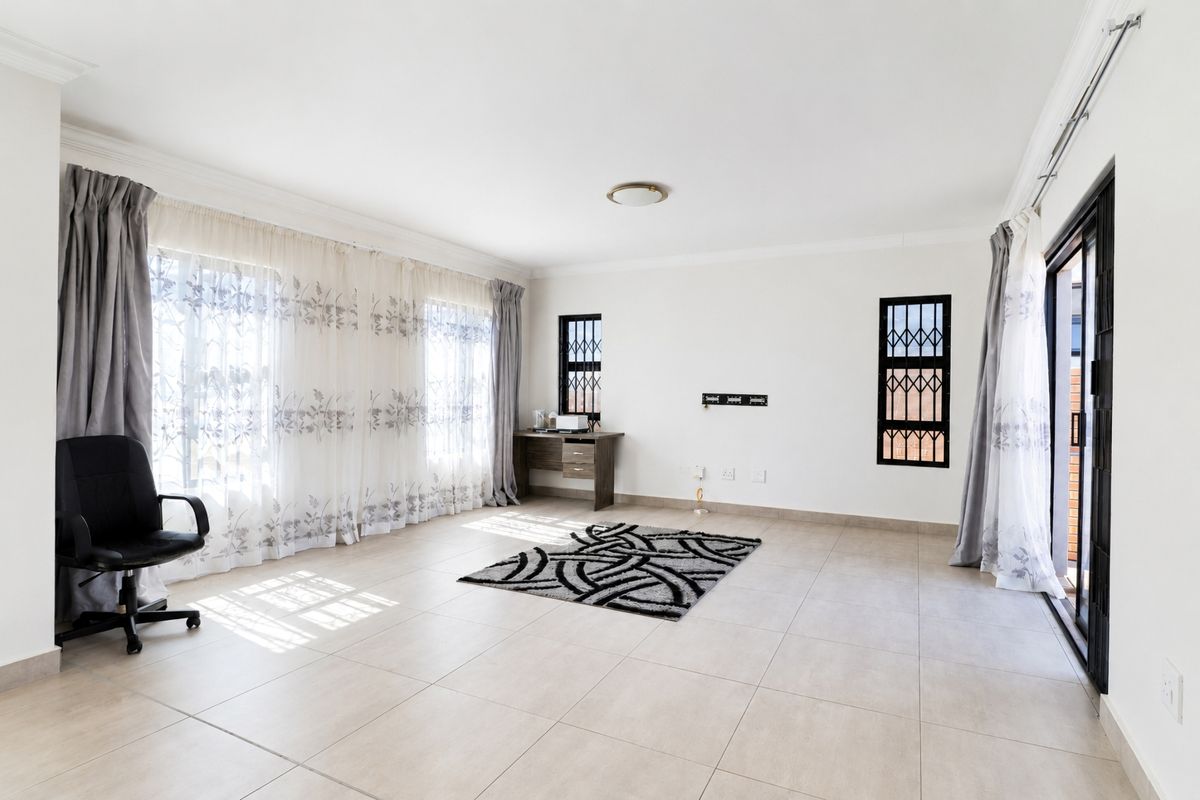 A bright and spacious living area featuring neutral tiled flooring, large windows with security gates, and a sliding door leading to the exterior.