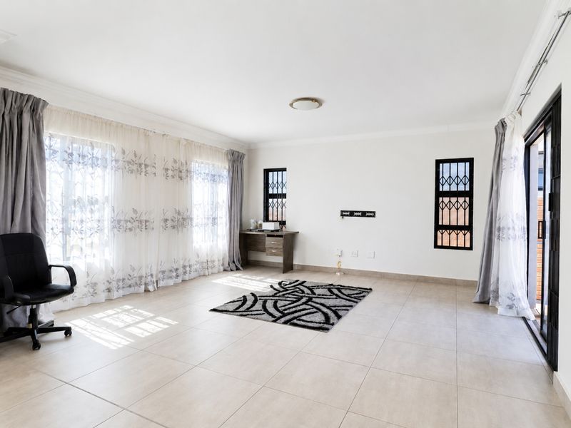 A bright and spacious living area featuring neutral tiled flooring, large windows with security gates, and a sliding door leading to the exterior.
