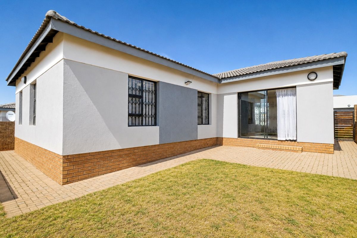 Rear view of the property featuring a paved patio area, a small lawn, and a sliding glass door with security bars.