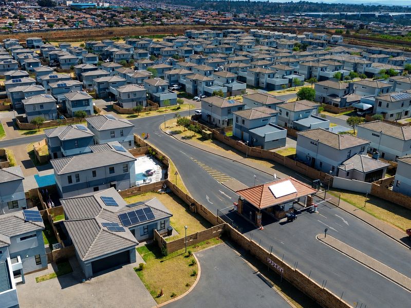 Aerial view of a modern residential estate featuring uniform housing units, paved streets, and a secure gated entrance.