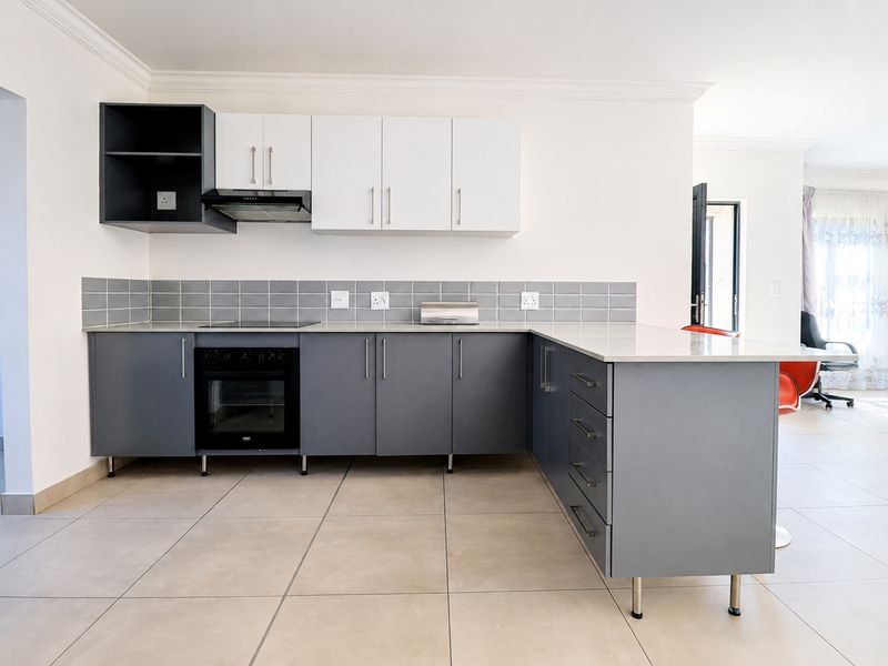 Modern kitchen featuring grey and white cabinetry, quartz countertops, built-in oven, electric hob, and neutral ceramic floor tiles.