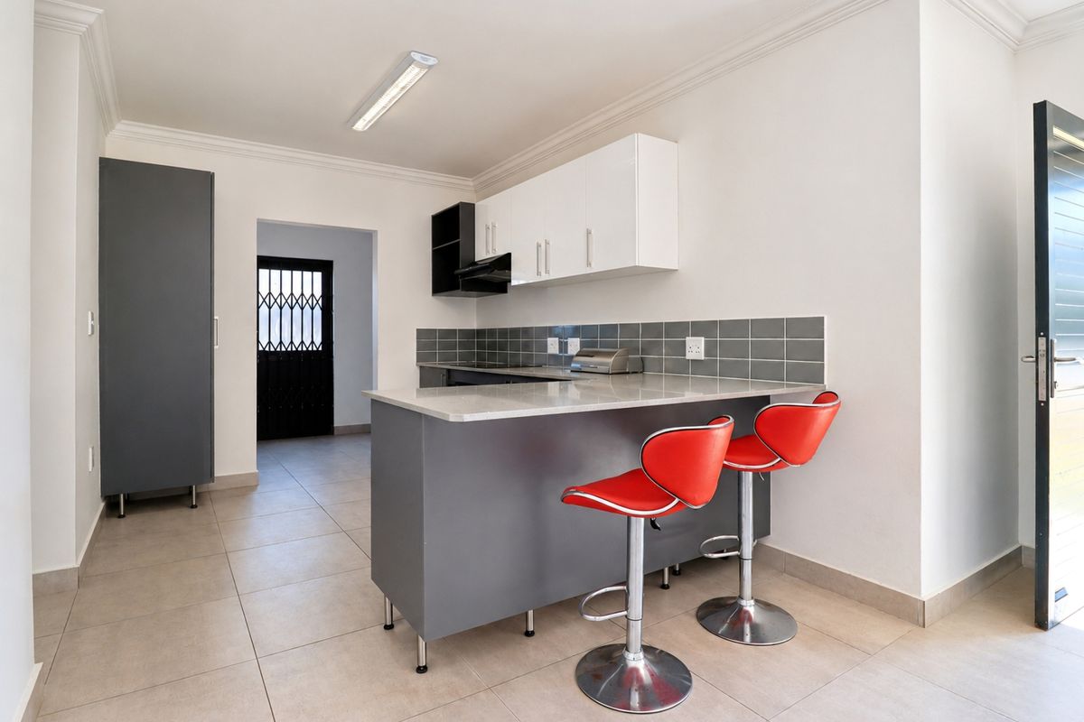 Modern kitchen featuring a breakfast bar, stone countertops, grey and white cabinetry, tiled backsplash, and ceramic floor tiles.