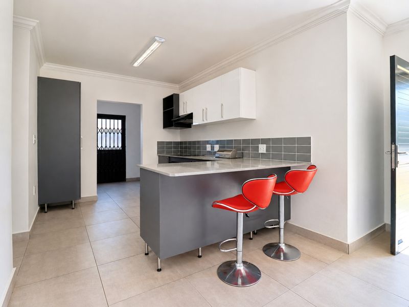 Modern kitchen featuring a breakfast bar, stone countertops, grey and white cabinetry, tiled backsplash, and ceramic floor tiles.