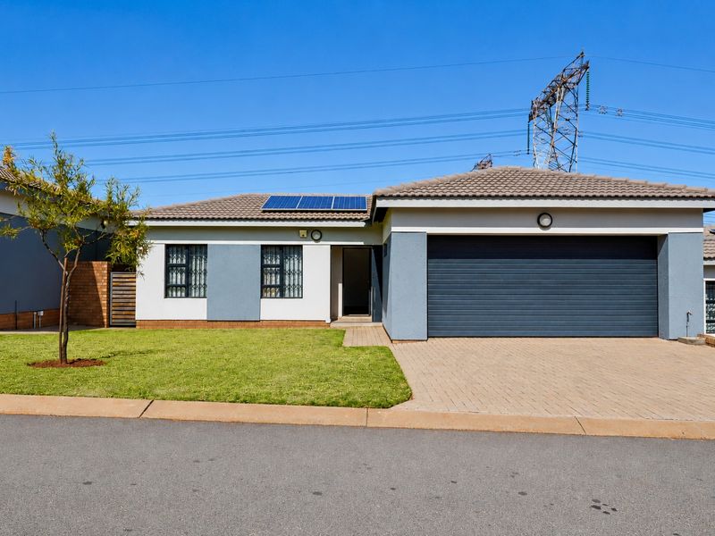 Front elevation of a modern single-story house featuring a paved driveway, double garage, and roof-mounted solar panels.