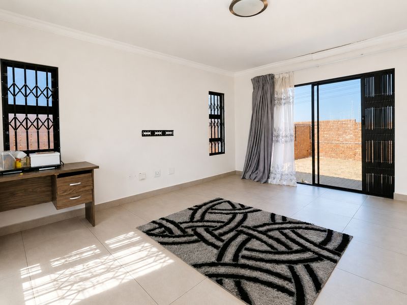 A bright, open-plan living area featuring neutral tiled flooring, security gates on windows and doors, and direct access to the rear outdoor space.