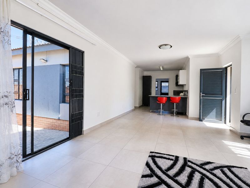 An open-plan living and kitchen area featuring neutral tiled flooring, a kitchen island with breakfast bar, and large sliding doors leading to the exterior.