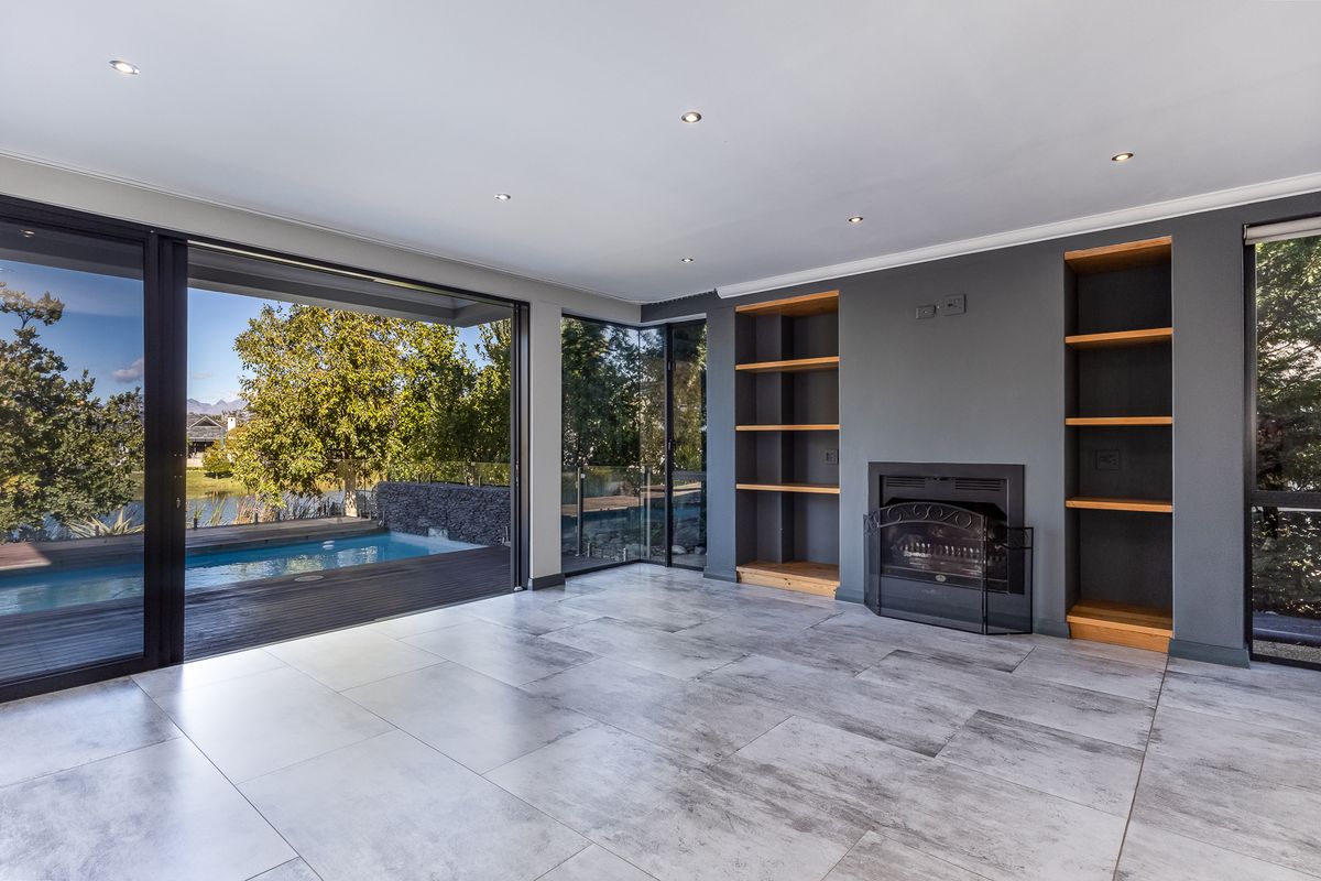 Spacious living area featuring modern tiled floors, built-in fireplace, custom shelving, and seamless access to the outdoor pool deck through large sliding glass doors.
