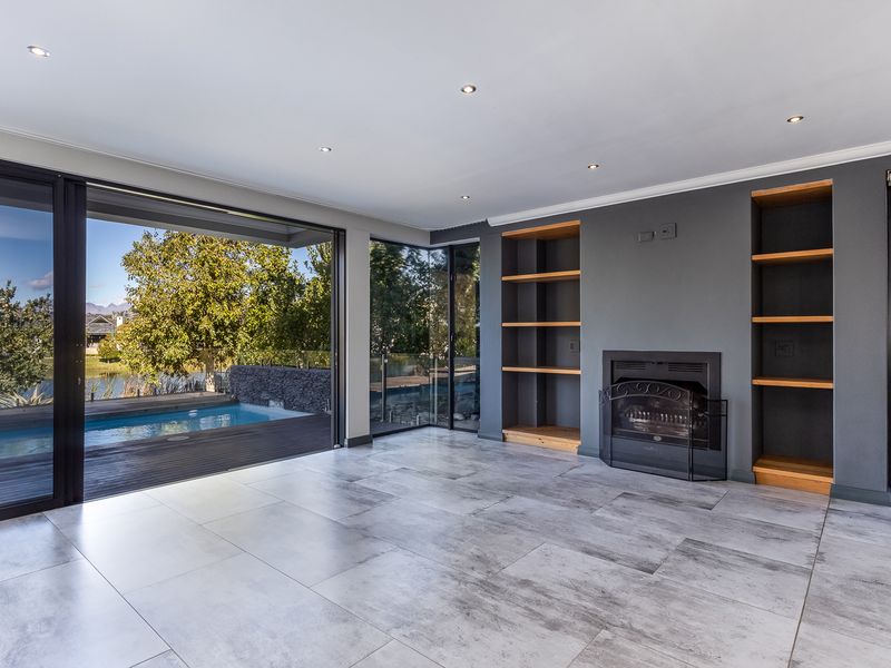Spacious living area featuring modern tiled floors, built-in fireplace, custom shelving, and seamless access to the outdoor pool deck through large sliding glass doors.