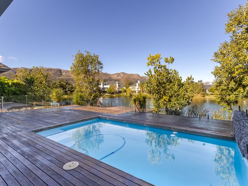 Outdoor pool area featuring timber decking, glass balustrades, and a stone feature wall, overlooking a scenic lake and mountain backdrop.