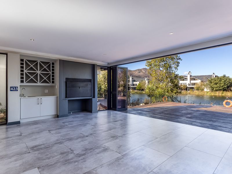 Spacious open-plan living area featuring a built-in braai, kitchenette with wine storage, and seamless flow to a timber deck overlooking the lake.