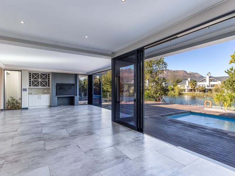Spacious open-plan living area featuring a built-in bar and fireplace, with seamless flow through stacking doors to a timber deck and swimming pool.