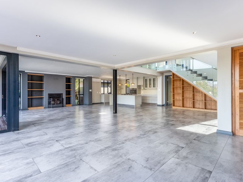 Spacious open-plan living and kitchen area featuring modern tiled floors, a built-in fireplace, custom shelving, and a sleek staircase with glass balustrades.