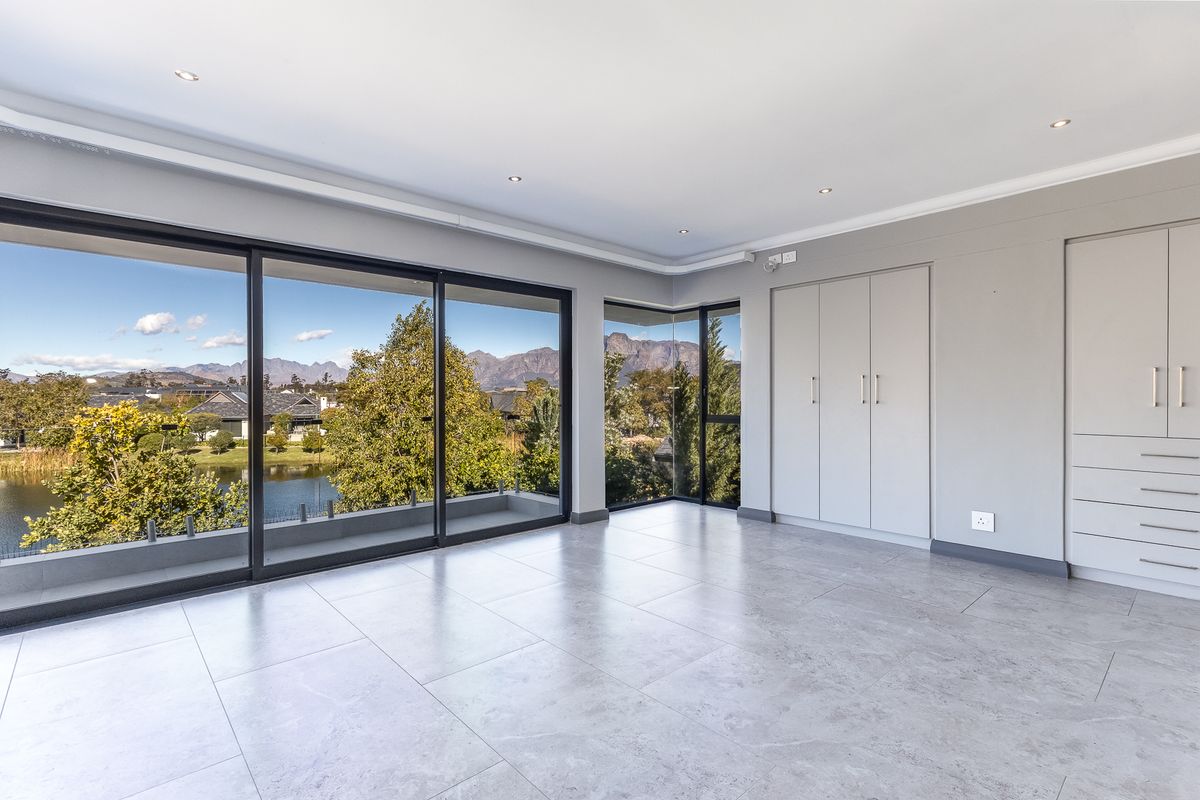 Spacious, modern bedroom featuring large sliding glass doors with scenic mountain and lake views, built-in cupboards, and neutral tiled flooring.
