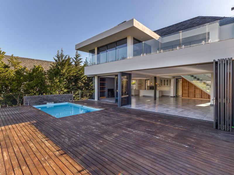 Rear view of a modern residence featuring a swimming pool, extensive timber decking, and large bi-fold doors opening into an open-plan living area.