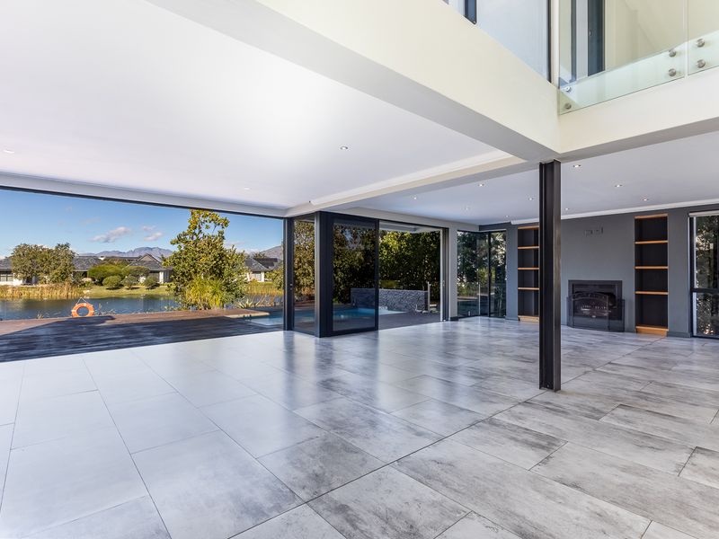 Spacious open-plan living area featuring large format tiles, a built-in fireplace, and seamless indoor-outdoor flow through expansive sliding glass doors overlooking the water.