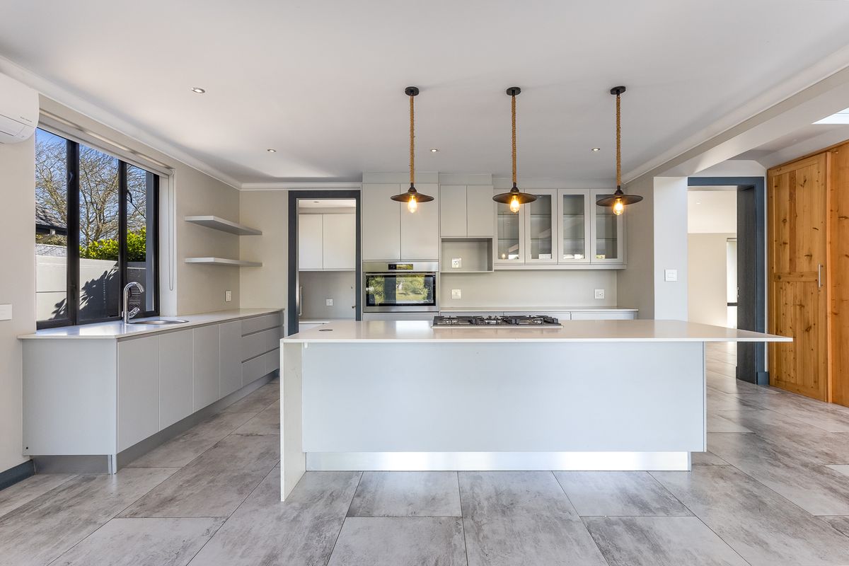 Modern kitchen featuring a large central island with gas cooktop, stone countertops, built-in oven, and sleek cabinetry, complemented by stylish pendant lighting.