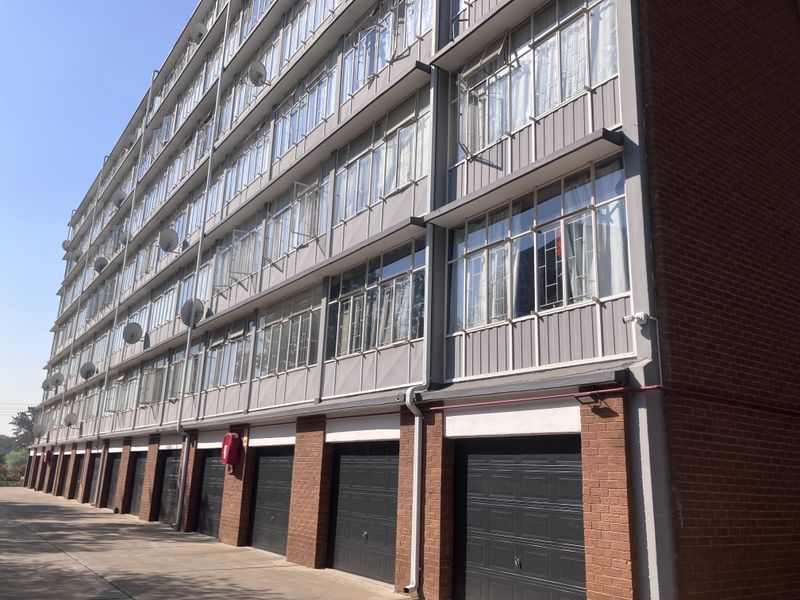 Exterior view of a multi-story apartment building featuring a brick facade, rows of metal-framed windows, and ground-level sectional garage doors.