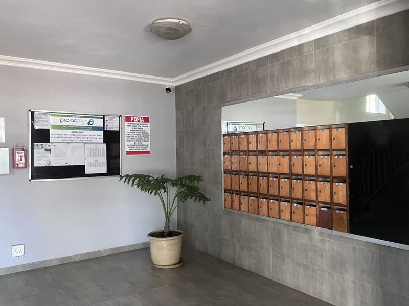 A clean and functional apartment building entrance lobby featuring a wall of built-in wooden mailboxes and tiled flooring.