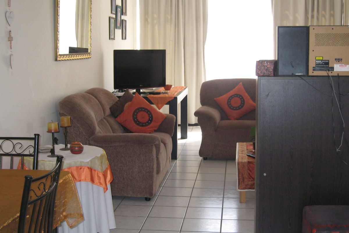 A living room area featuring tiled flooring and large windows with curtains, providing a functional space for relaxation.