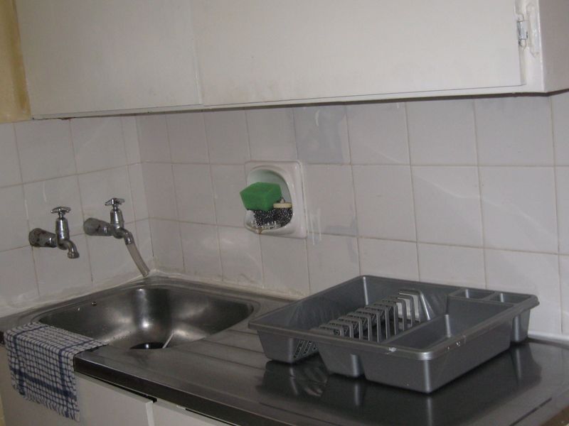 A dated kitchen sink area featuring a stainless steel basin, tiled backsplash, and wall-mounted cabinetry in need of modernization.