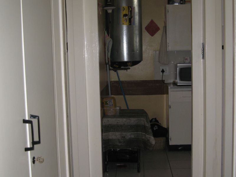 A compact scullery or utility area featuring built-in cabinetry, tiled flooring, and an exposed electric water heater.