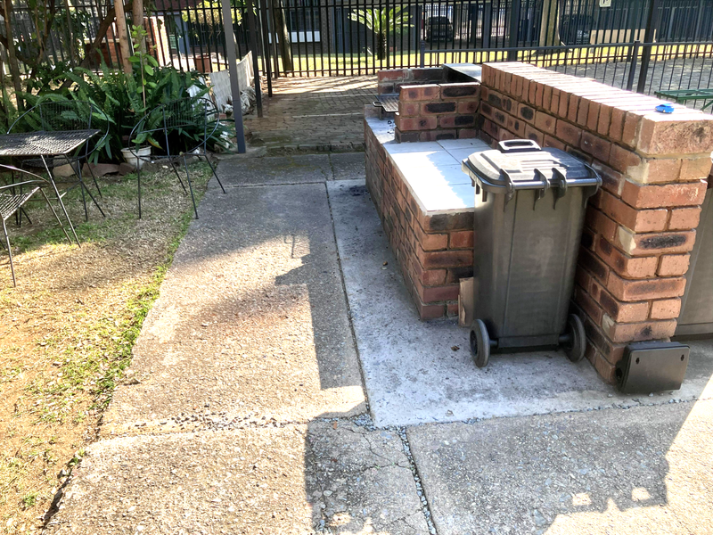 Outdoor patio area featuring a built-in brick braai and concrete paving, enclosed by metal perimeter fencing.