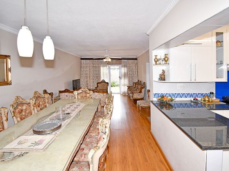 Open-plan living and dining area featuring laminate flooring, crown molding, and a functional kitchen with granite countertops and modern pendant lighting.