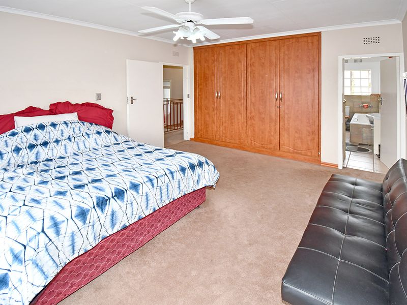 Spacious bedroom featuring built-in wooden cupboards, a ceiling fan, and direct access to an en-suite bathroom.
