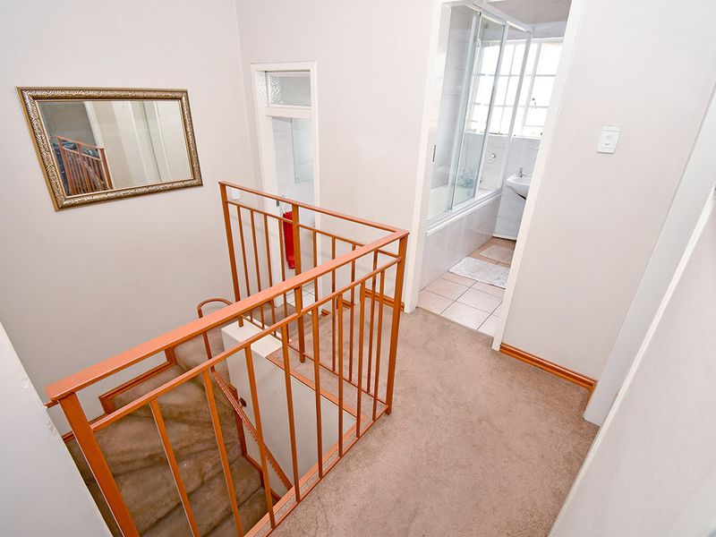 Upper level landing area featuring carpeted flooring and a metal staircase railing, providing access to the adjacent bathroom.