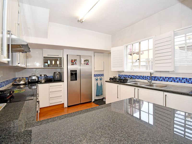 A functional kitchen featuring granite countertops, white cabinetry, a stainless steel double sink, and a tiled backsplash with integrated appliances.