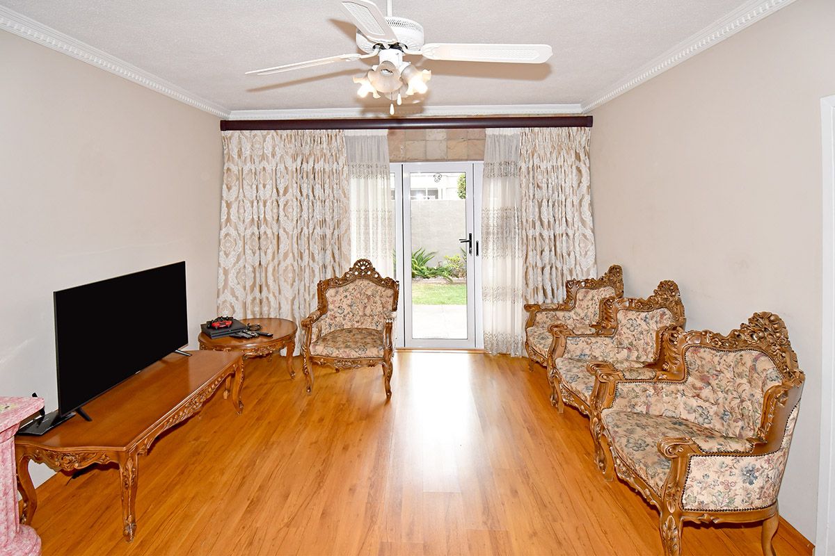 A living room featuring laminate flooring, a ceiling fan, crown molding, and a glass sliding door providing access to the rear garden.