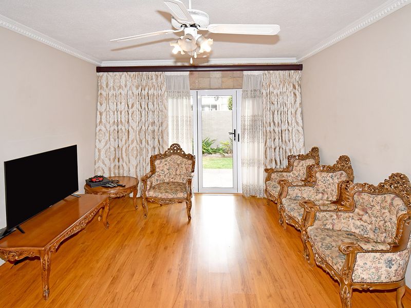 A living room featuring laminate flooring, a ceiling fan, crown molding, and a glass sliding door providing access to the rear garden.