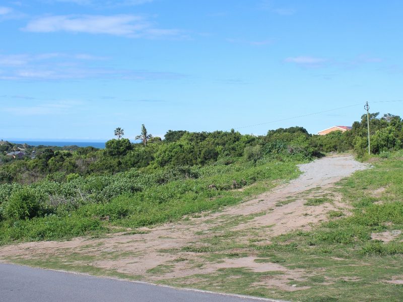 A vacant residential plot featuring a natural landscape, unpaved access path, and distant coastal views.