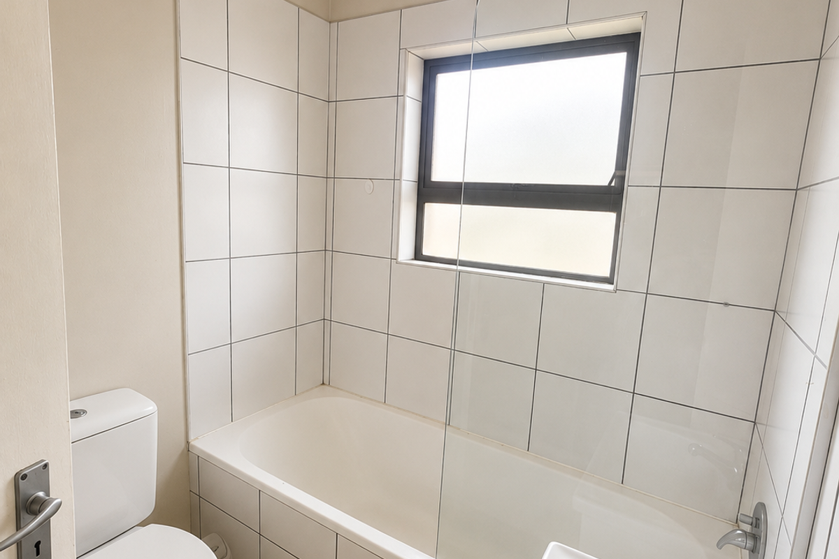 A clean, functional bathroom featuring a bathtub with a glass shower screen, a toilet, and a pedestal washbasin with tiled finishes.