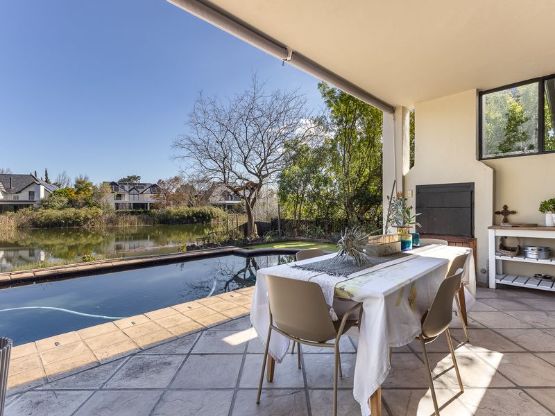 Covered patio featuring a built-in braai, tiled flooring, and direct access to a swimming pool with scenic water views.