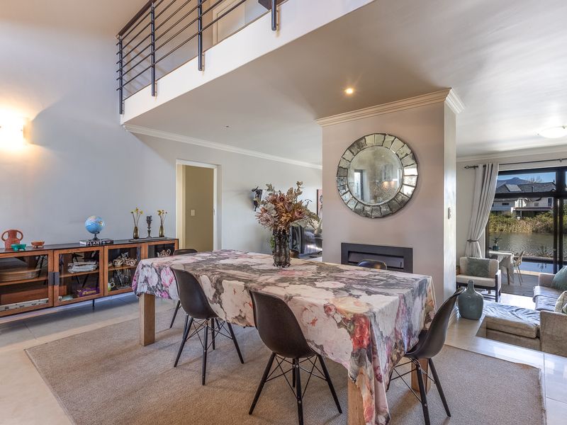 Spacious open-plan living and dining area featuring a built-in fireplace, mezzanine level with metal balustrade, and large sliding doors opening to a scenic view.