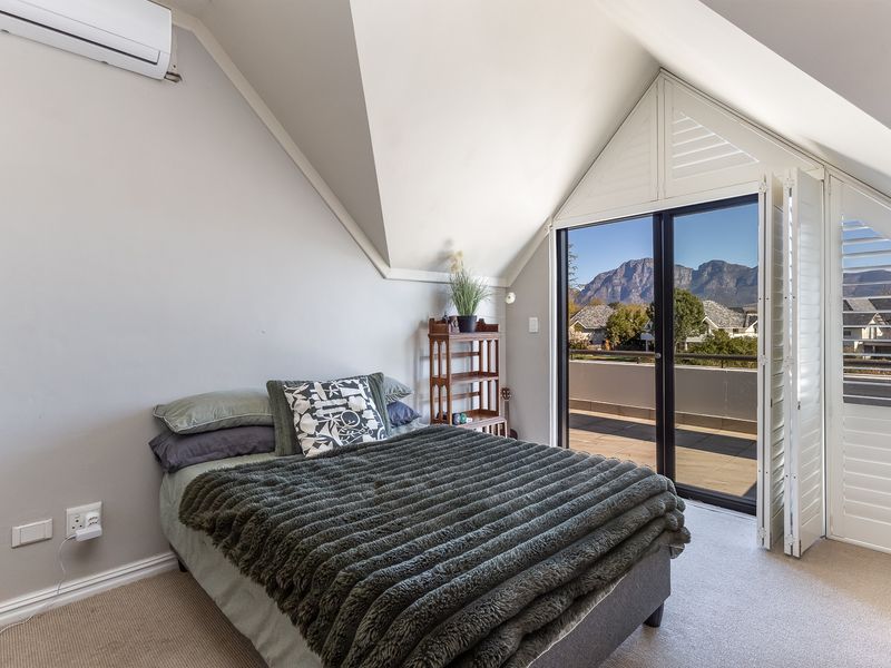 A bright bedroom featuring a sloped ceiling, split-system air conditioning, and sliding glass doors that open onto a balcony with mountain views.