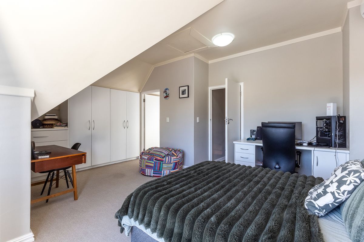 A spacious bedroom featuring built-in cupboards, a built-in desk area, and a unique sloped ceiling design with neutral wall finishes.