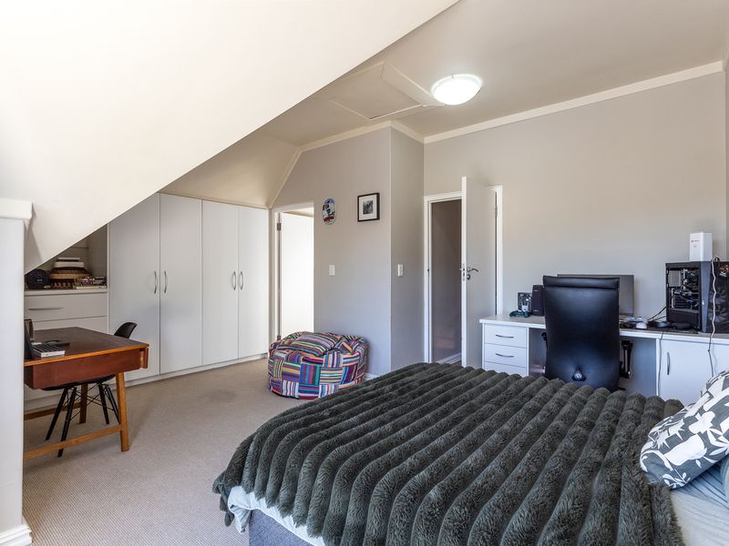 A spacious bedroom featuring built-in cupboards, a built-in desk area, and a unique sloped ceiling design with neutral wall finishes.
