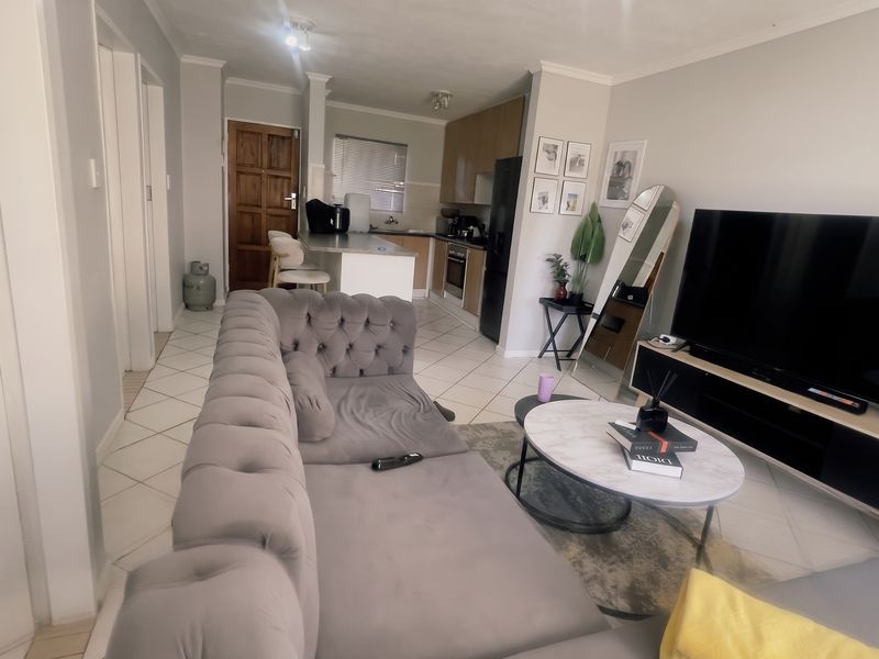An open-plan living area featuring tiled flooring, a modern kitchen with built-in cabinetry, and a breakfast counter, seamlessly connecting to the lounge space.