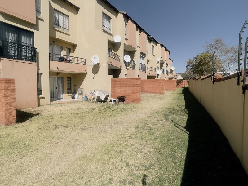 Rear view of a multi-story apartment complex featuring private brick-walled garden sections, balconies, and a perimeter wall with electric security fencing.