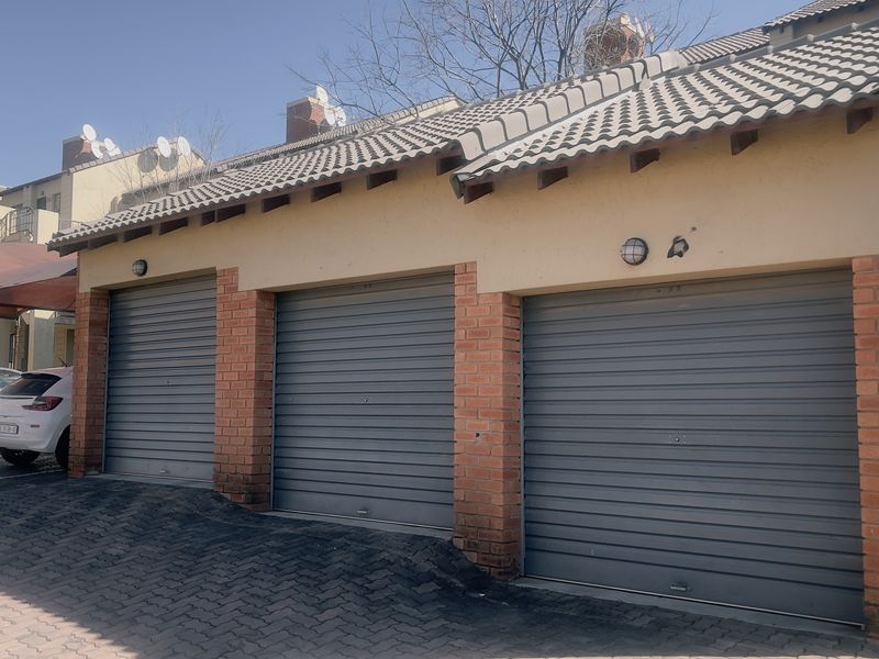 A triple garage unit featuring roller shutter doors, brick pillar detailing, and a tiled roof, situated within a paved residential complex.