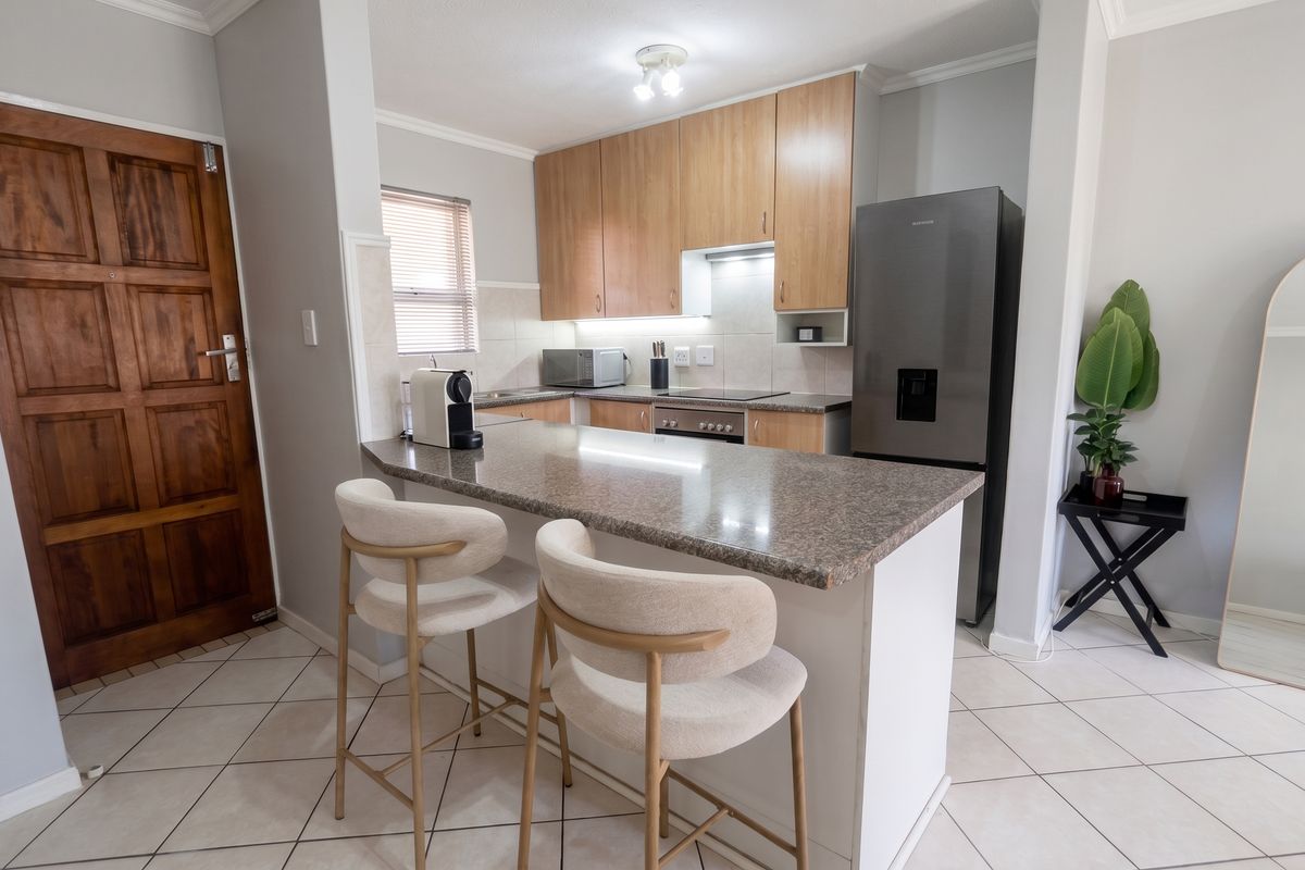 A functional kitchen featuring granite countertops, built-in cabinetry, an electric hob, and a breakfast nook, finished with tiled flooring.