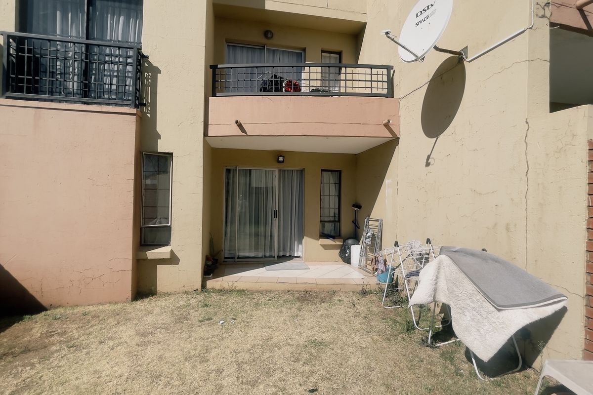 Rear view of the apartment featuring a small patio, balcony above, and a private garden area with a brick boundary wall.