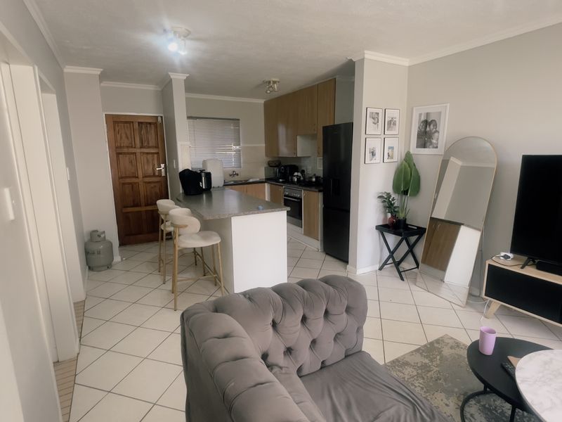Open-plan living area featuring a functional kitchen with wood-finish cabinetry, a breakfast island, and tiled flooring throughout the combined space.